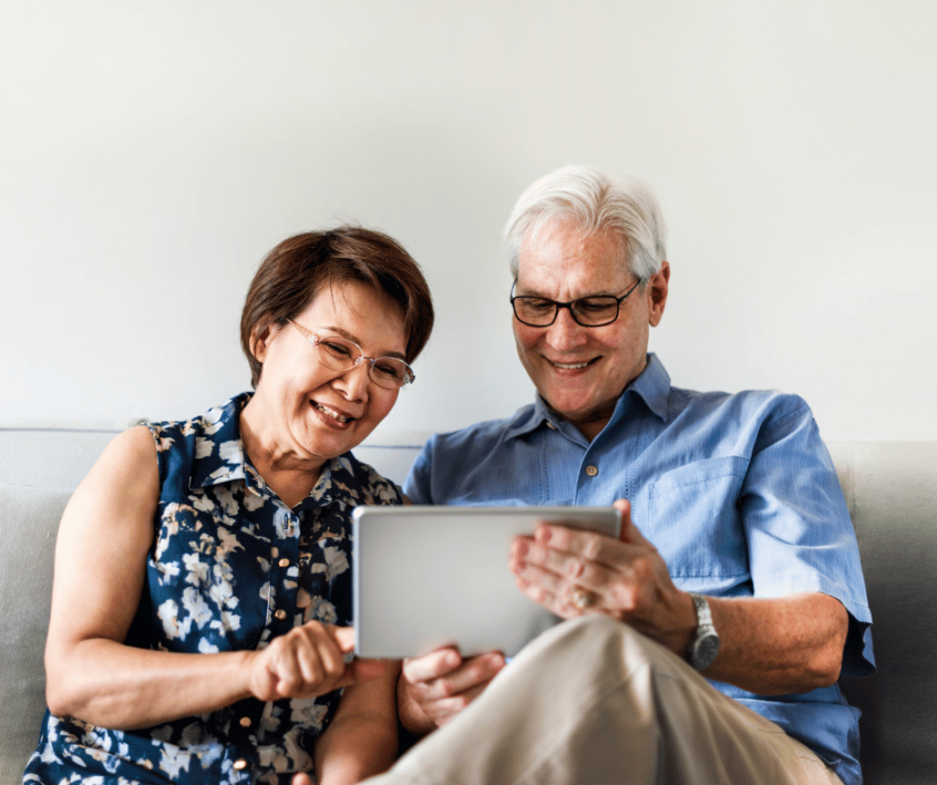 Image of a couple smiling while sitting on their couch using a tablet.